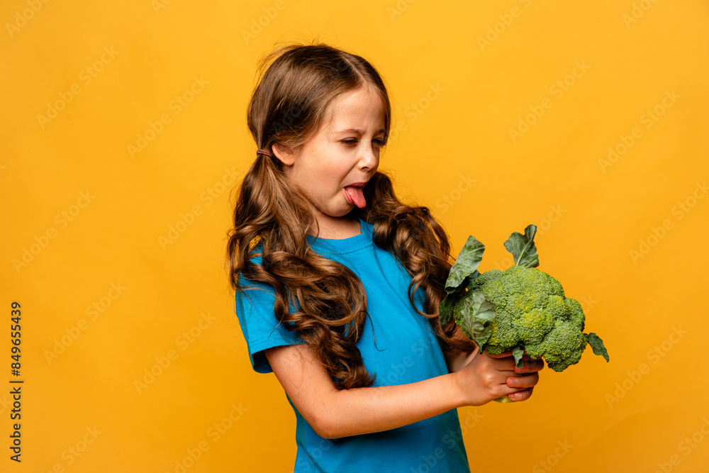 Little cute kid girl refusing to eat healthy vegetables broccoli on yellow background. Children do not like to eat vegetables. Little cute kid girl refusing to eat healthy vegetables broccoli on yellow background. Children do not like to eat vegetables.