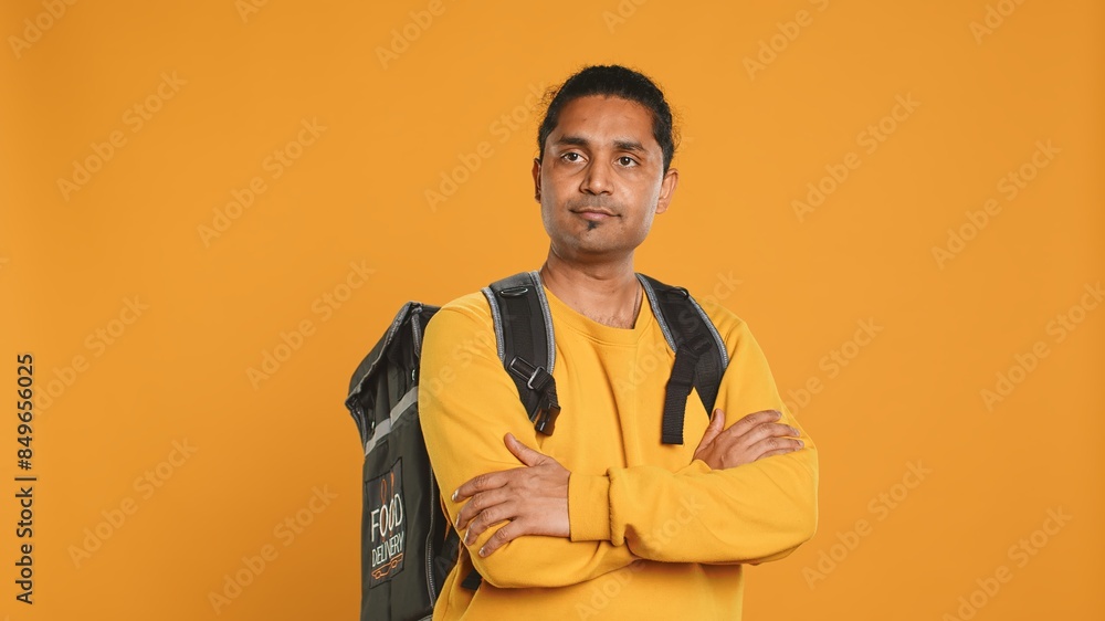 Portrait of upbeat indian man holding thermal backpack, isolated over studio background. Friendly cheerful person prepared to deliver takeaway food to customers, camera A