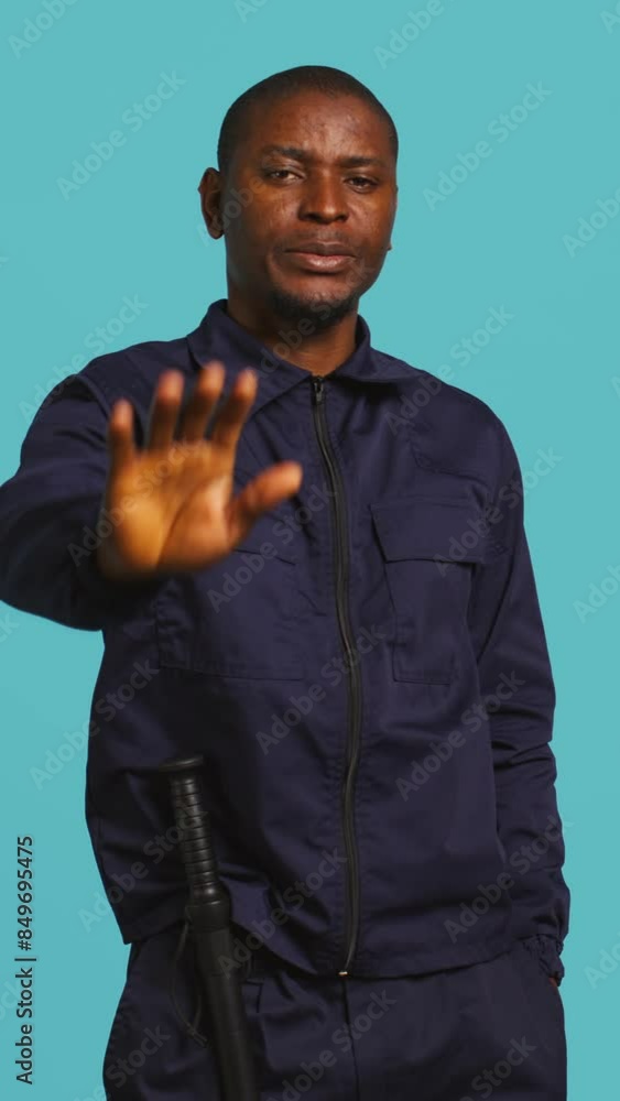 Vertical video Security guard doing stop sign gesturing, being tasked with preventing criminal activity and detaining suspects. Portrait of stern bodyguard showing halt hand gesture, studio background Vertical video Security guard doing stop sign gesturing, being tasked with preventing criminal activity and detaining suspects. Portrait of stern bodyguard showing halt hand gesture, studio background