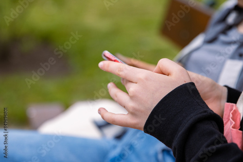 Thumb finger on screen of mobile phone. Person texting text message, hipster touch smartphone screen. Girl hands holding scrolling chatting working. Summer park. Close up. Copy space. Selective focus © Dina