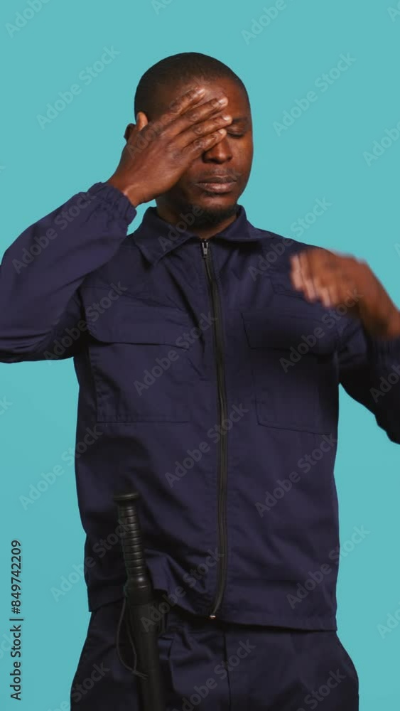 Vertical video Portrait of tired security guard suffering from painful headache while overseeing premises. Private law enforcement worker feeling ache from fatigue, studio backdrop, camera B Vertical video Portrait of tired security guard suffering from painful headache while overseeing premises. Private law enforcement worker feeling ache from fatigue, studio backdrop, camera B
