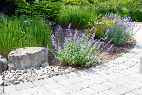 Low maintenance front garden landscaping features decorative armour stone and river rock, no lawn and easy care perennial hosta and ornamental grasses for colour and texture.