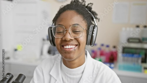 Smiling african american woman scientist with headphones analyzing samples in laboratory photo