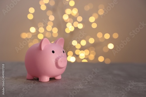 Pink piggy bank on grey table against blurred lights, space for text