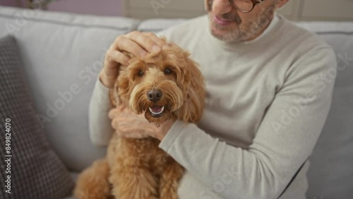 A middle-aged man in glasses affectionately pets his happy poodle indoors, providing a warm and cozy home setting. photo