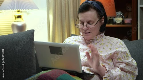 A mature woman, with dark hair, in a nightgown, communicates with a locher on a tablet, sitting on the sofa, covered with a blanket, in a quiet, homely environment. Slow motion. photo