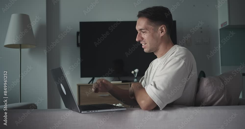 Seated on couch man works on laptop face lighting up with sense of accomplishment success complete tasks. Laptop work mid adult male sitting couch celebrate success fist up emotion happiness success. Seated on couch man works on laptop face lighting up with sense of accomplishment success complete tasks. Laptop work mid adult male sitting couch celebrate success fist up emotion happiness success.