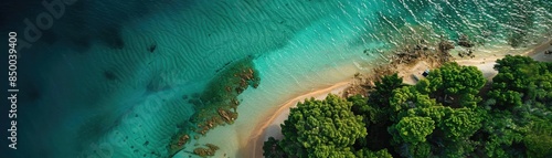 Aerial view of a beautiful tropical beach with clear turquoise water and lush green forest in the background.