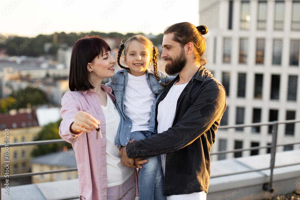 Happy family celebrating new house key on rooftop terrace in urban setting. Smiling parents with child enjoying momentous occasion. Happy family celebrating new house key on rooftop terrace in urban setting. Smiling parents with child enjoying momentous occasion.