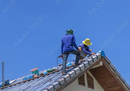 Repairmans repairing leaking ridges tile roofing and replace cracked broken tile roofing on  blue  sky  background.