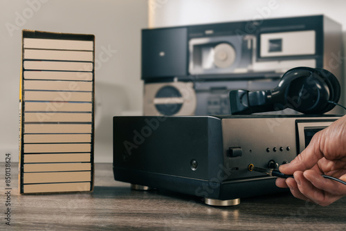 Male music lover connecting headphones jack to vintage audio cassette player. Vintage cassette recorder in a cozy room, prepared for a nostalgic music session with classic audio equipment