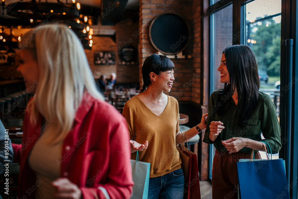 Fototapeta premium Smiling women with shopping bags entering a trendy restaurant, excited for a meal together