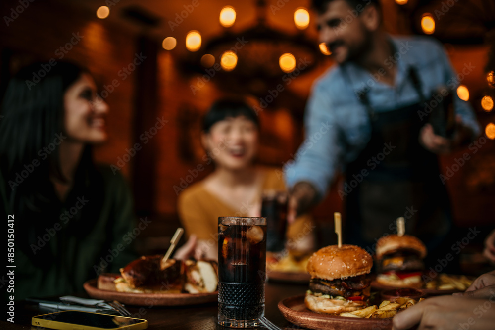 Two female friends are having fun while a waiter is serving them food and drinks in a pub