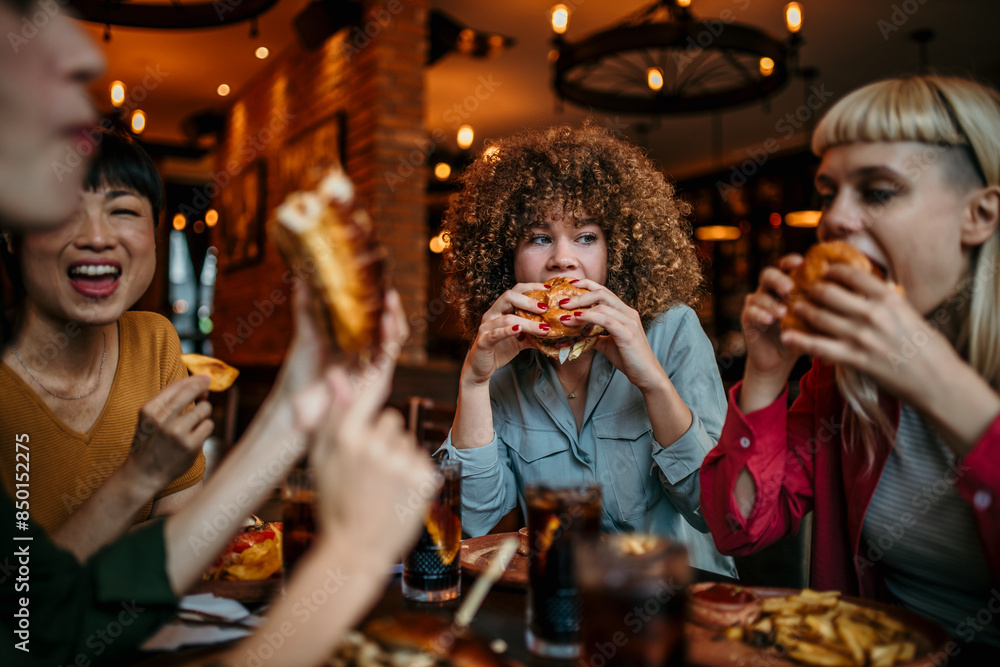 Fototapeta premium Hungry woman eating a burger while gathering with friends in a pub