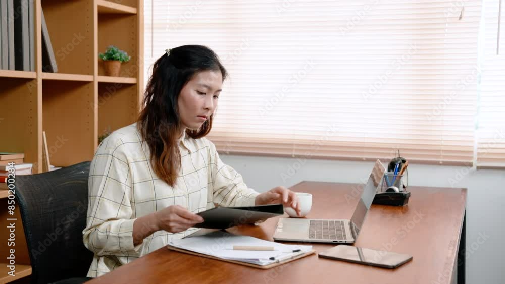 Asian woman, office worker, sitting in private office, open document folder, before turning typing data in document file is holding, into laptop computer, search for information obtained. Asian woman, office worker, sitting in private office, open document folder, before turning typing data in document file is holding, into laptop computer, search for information obtained.