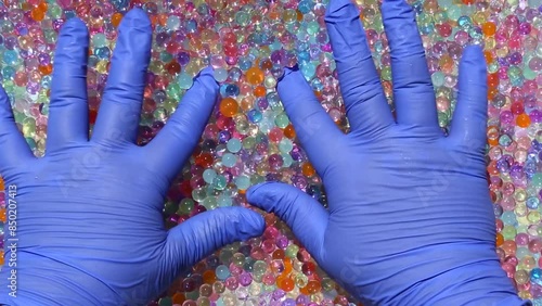 Hands in blue gloves are playing with multicolored orbis. Fingers dip and wiggle, pressing a multitude of colored orbis. Playful, uplifting. Asmr. Part7.14 photo