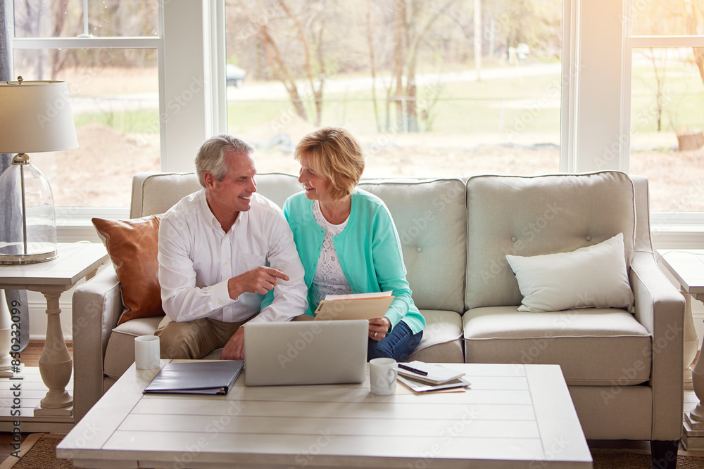 Senior couple, paperwork and laptop on couch with discussion, smile and point for taxes in home. Old man, woman and computer with documents for compliance, reading and investment report with finance Senior couple, paperwork and laptop on couch with discussion, smile and point for taxes in home. Old man, woman and computer with documents for compliance, reading and investment report with finance
