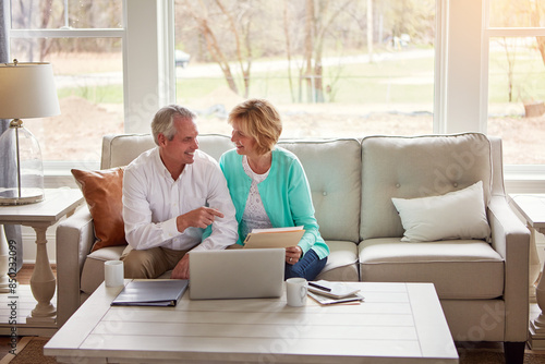 Senior couple, paperwork and laptop on couch with discussion, smile and point for taxes in home. Old man, woman and computer with documents for compliance, reading and investment report with finance © peopleimages.com