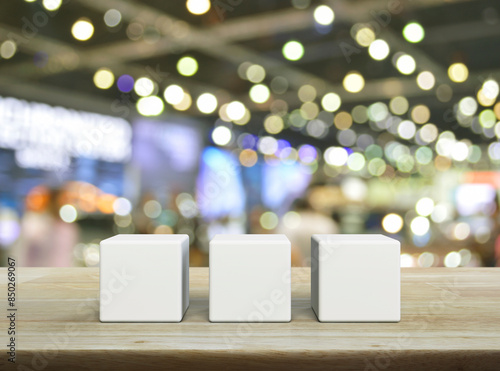 Three white block cubes on wooden table over blur light and shadow of shopping mall
