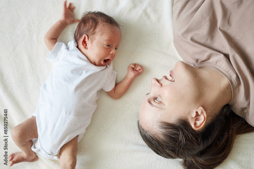 Beautiful young mother with newborn daughter or son in bodysuit enjoying time with her infant child with affection nursing her little kid with care Beautiful young mother with newborn daughter or son in bodysuit enjoying time with her infant child with affection nursing her little kid with care
