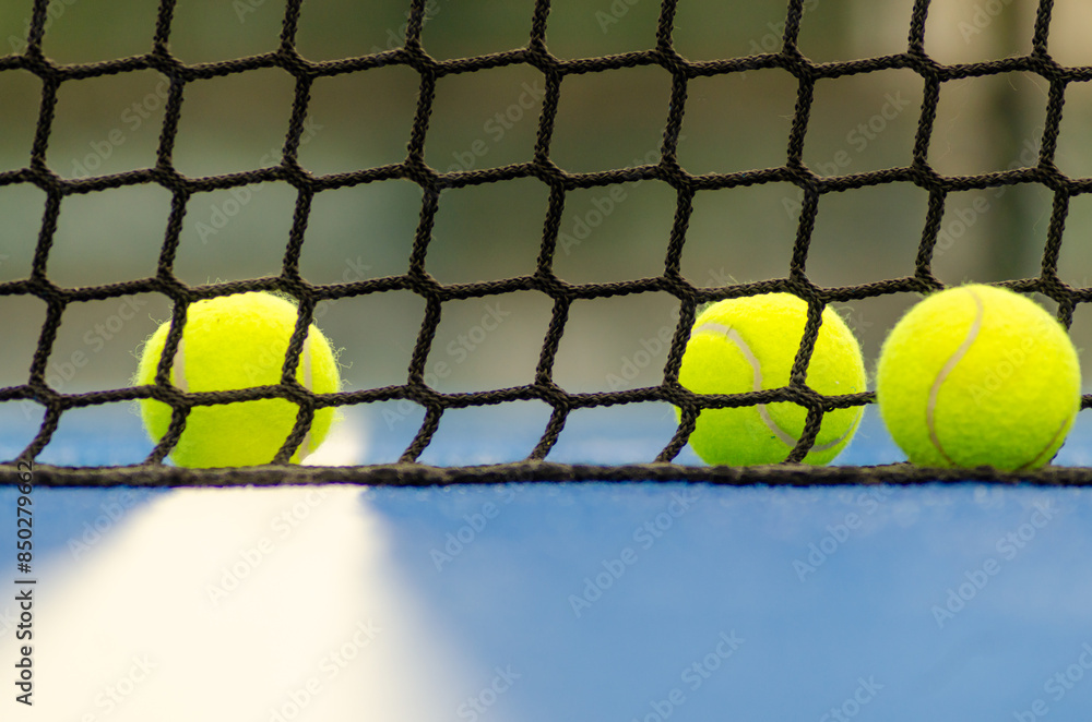 three balls next to the net of a blue paddle tennis court, defocused background three balls next to the net of a blue paddle tennis court, defocused background