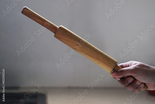 Woman’s hand holding belan or wooden roller or Brown Wooden Rolling Pin photo