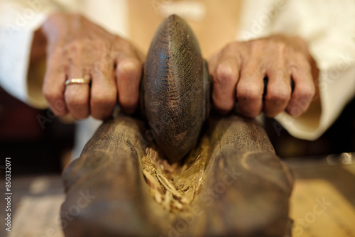 Obraz na plátně Close-up of senior man grinding ginger in ancient way for traditional Asian medi