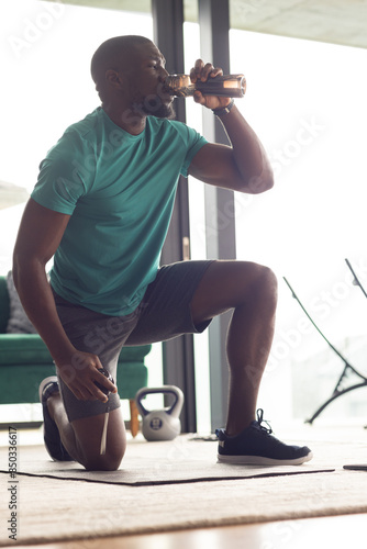 Fit African American male kneels, drinking water, relaxed post workout, living a healthy lifestyle photo