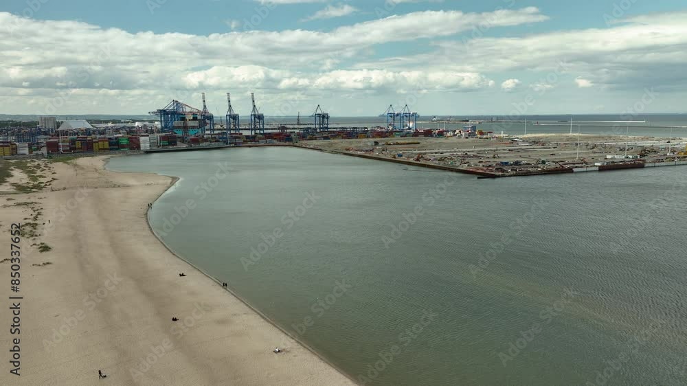 Aerial of a coastal industrial port with large cargo containers and cranes. The port's busy operations against a backdrop of a sandy beach and open sea, highlighting its key role in maritime logistics Aerial of a coastal industrial port with large cargo containers and cranes. The port's busy operations against a backdrop of a sandy beach and open sea, highlighting its key role in maritime logistics