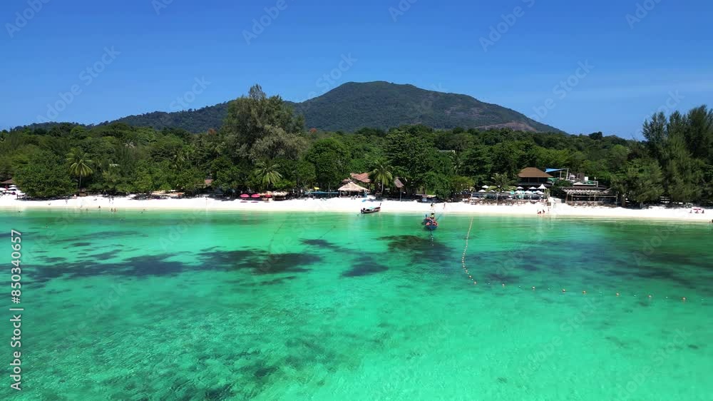 Tourists are enjoying a sunny day on a tropical island beach with traditional thai longtail boats moored in the turquoise water. Nice aerial view flight drone panorama overview drone