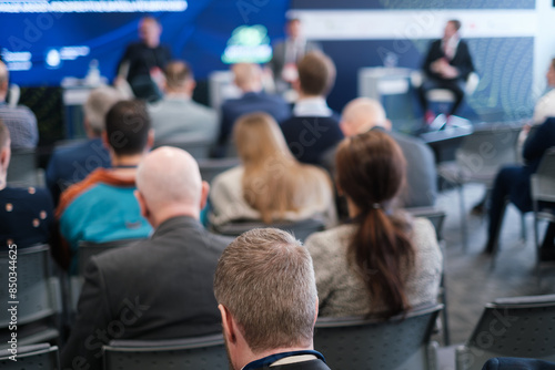 A business conference where audience members are attentively listening to speakers on stage. Professional setting with corporate discussions and networking.