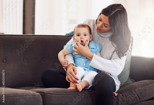 Family, mother and baby on sofa in living room, holding hands for love and playful for support. Smile, motherhood and toddler with woman together, hug and play by sitting for relationship at home