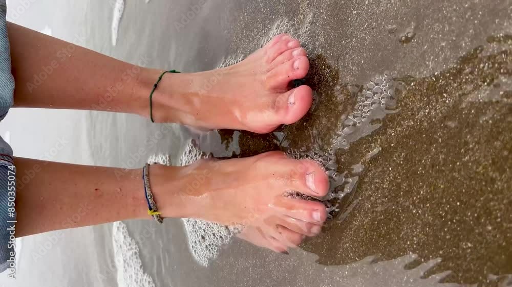 Bare feet standing on wet sand with ocean waves foaming around toes Bare feet standing on wet sand with ocean waves foaming around toes