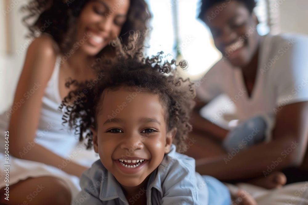A young child smiles broadly at the camera, while their parents sit behind them and out of focus A young child smiles broadly at the camera, while their parents sit behind them and out of focus