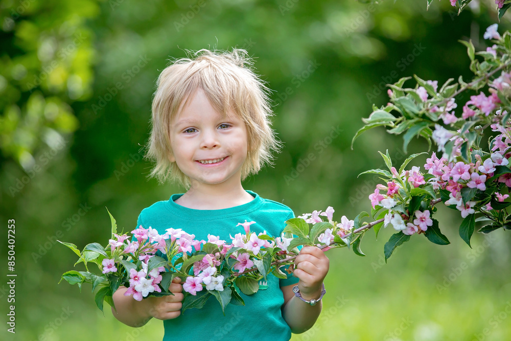 Cute little toddler child, standing next to a beautiful flower bush in spring Cute little toddler child, standing next to a beautiful flower bush in spring