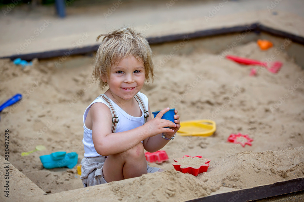 Cute toddler child, blond boy, playing in the sandpit in the park Cute toddler child, blond boy, playing in the sandpit in the park