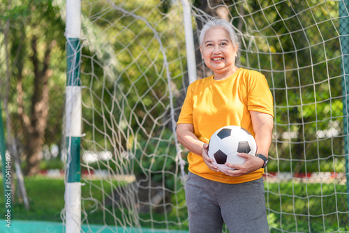 Active senior woman playing football in the urban outdoor court, Asian senior woman with a soccer ball, healthy life concepts