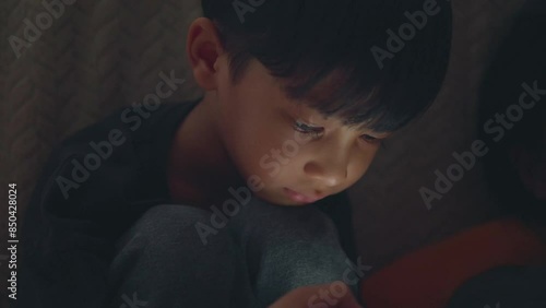 Asian boy is sitting using mobile phone in dark room and light comes from his mobile phone. internet, smart Phone addiction concept