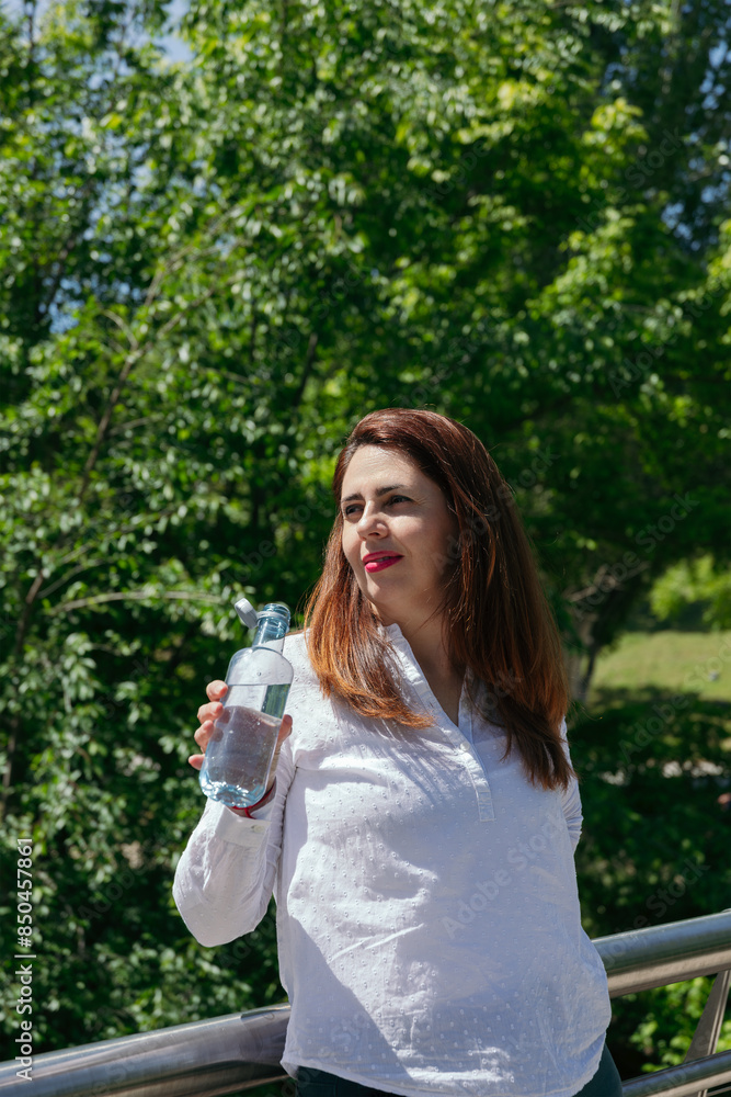 Portrait of a mature woman with long hair and red lips in nature drinking a bottle of water after a walk on a sunny day. Copy space. Healthy lifestyle concept Portrait of a mature woman with long hair and red lips in nature drinking a bottle of water after a walk on a sunny day. Copy space. Healthy lifestyle concept