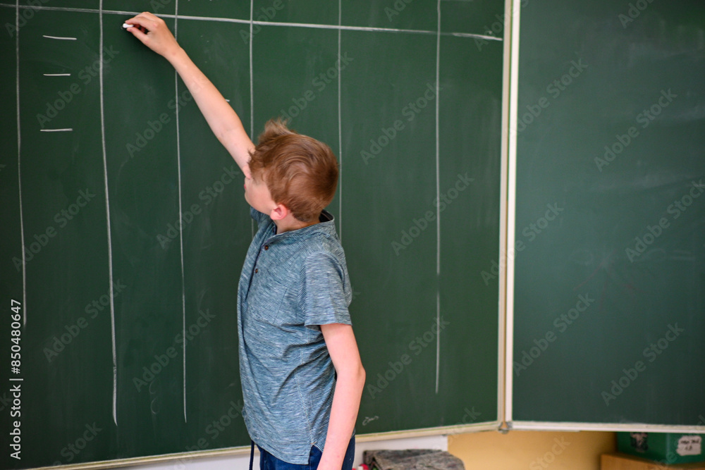 Young student is writing on a large green chalkboard while solving a math problem Young student is writing on a large green chalkboard while solving a math problem