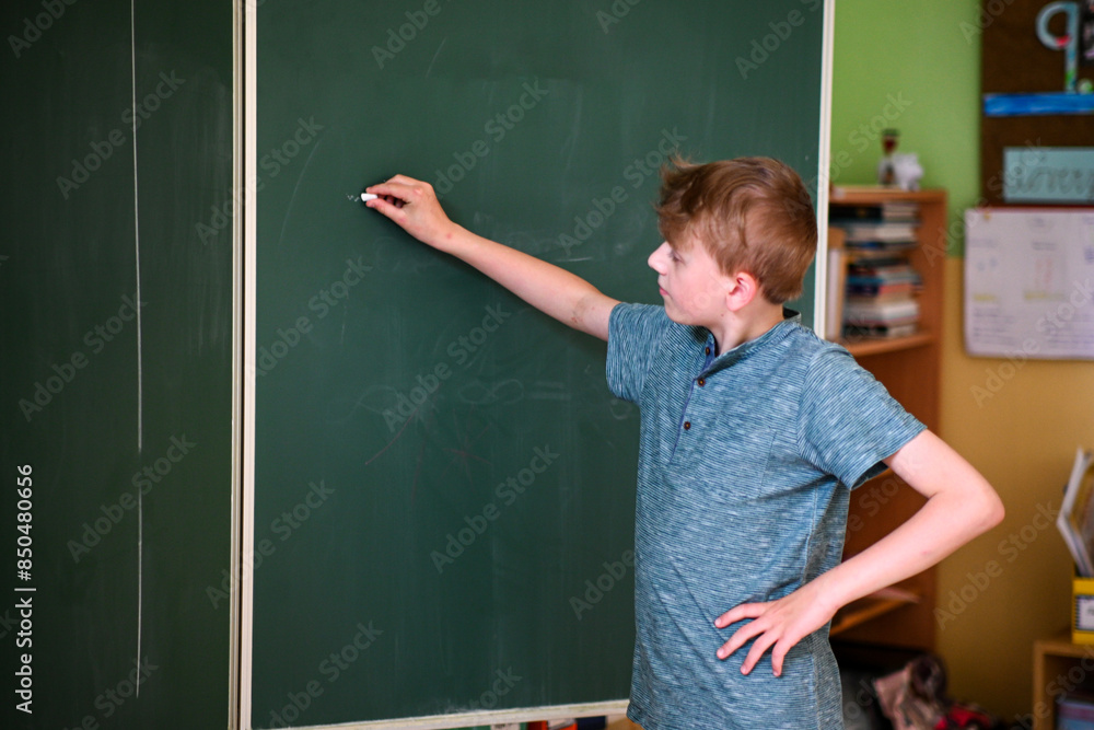 Young student is writing on a large green chalkboard while solving a math problem Young student is writing on a large green chalkboard while solving a math problem