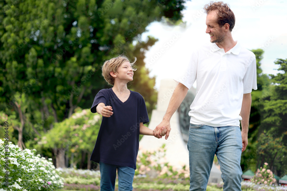 Father and son holding hands while walking in the park. Happy family, parent and kid spending time outdoors together in beautiful garden on holiday. little boy child playing with father outside. Father and son holding hands while walking in the park. Happy family, parent and kid spending time outdoors together in beautiful garden on holiday. little boy child playing with father outside.