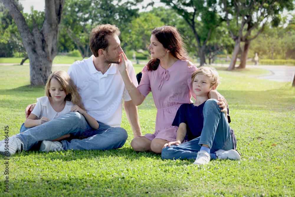 Happy family sitting on green grass at the park, smiling father, mother, son and daughter spending time together outdoors in beautiful garden on weekend holiday. Parents and kids have fun outside. Happy family sitting on green grass at the park, smiling father, mother, son and daughter spending time together outdoors in beautiful garden on weekend holiday. Parents and kids have fun outside.