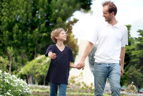 Father and son holding hands while walking in the park. Happy family, parent and kid spending time outdoors together in beautiful garden on holiday. little boy child playing with father outside. © Stella