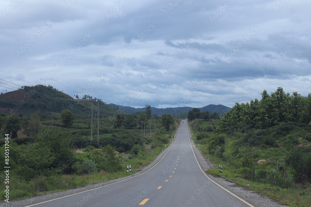 A long, straight road cuts through a valley framed by distant mountains. Trees line the roadside, adding a touch of green to the scene. A long, straight road cuts through a valley framed by distant mountains. Trees line the roadside, adding a touch of green to the scene.