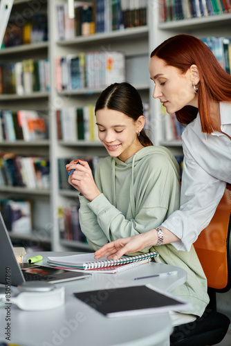 Obraz na płótnie A tutor with red hair teaches a teenage girl in a library, as they work together on a laptop for their modern education
