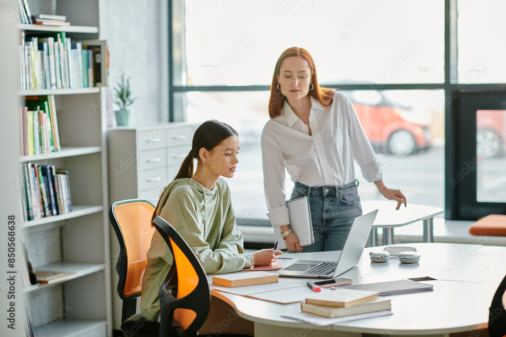 A redhead tutor and a teenage girl work together at a desk in an office, engaging in after-school lessons with the aid of laptops. A redhead tutor and a teenage girl work together at a desk in an office, engaging in after-school lessons with the aid of laptops.