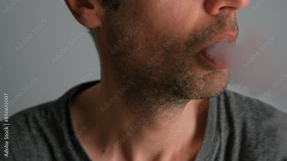 Close-up of a man smoking an electronic cigarette and exhaling smoke. Close-up of a man smoking an electronic cigarette and exhaling smoke.