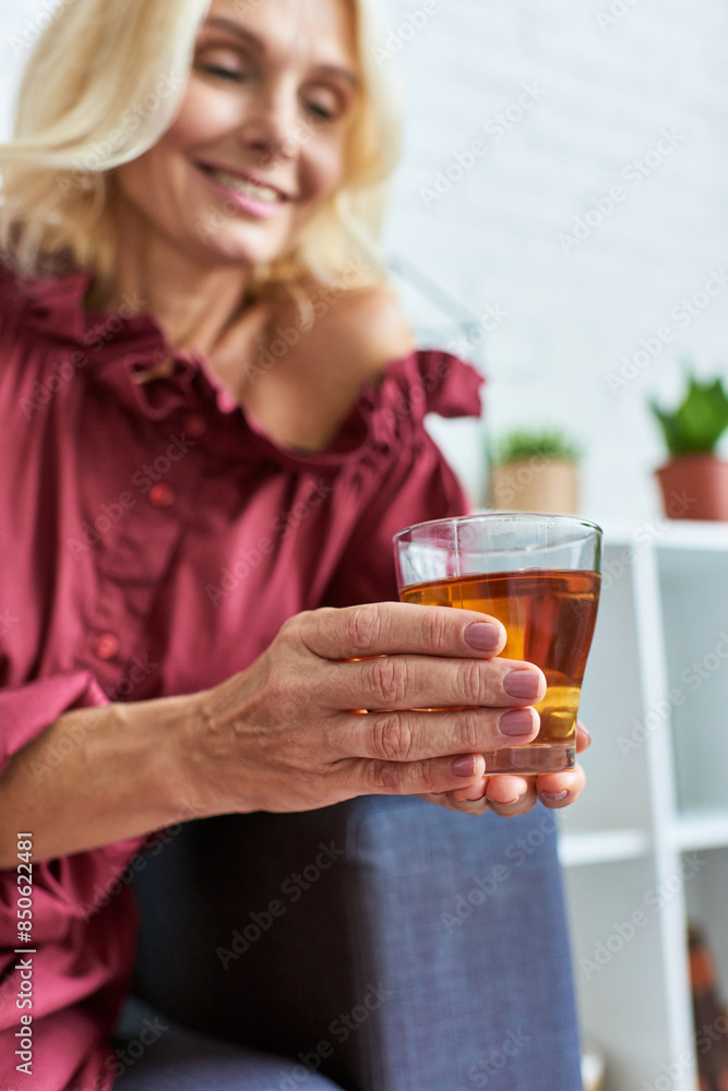 Mature woman in stylish dress relaxes on couch, holding glass of tea. Mature woman in stylish dress relaxes on couch, holding glass of tea.