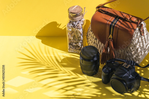 Camera, lens, straw bag and shells on a yellow background.